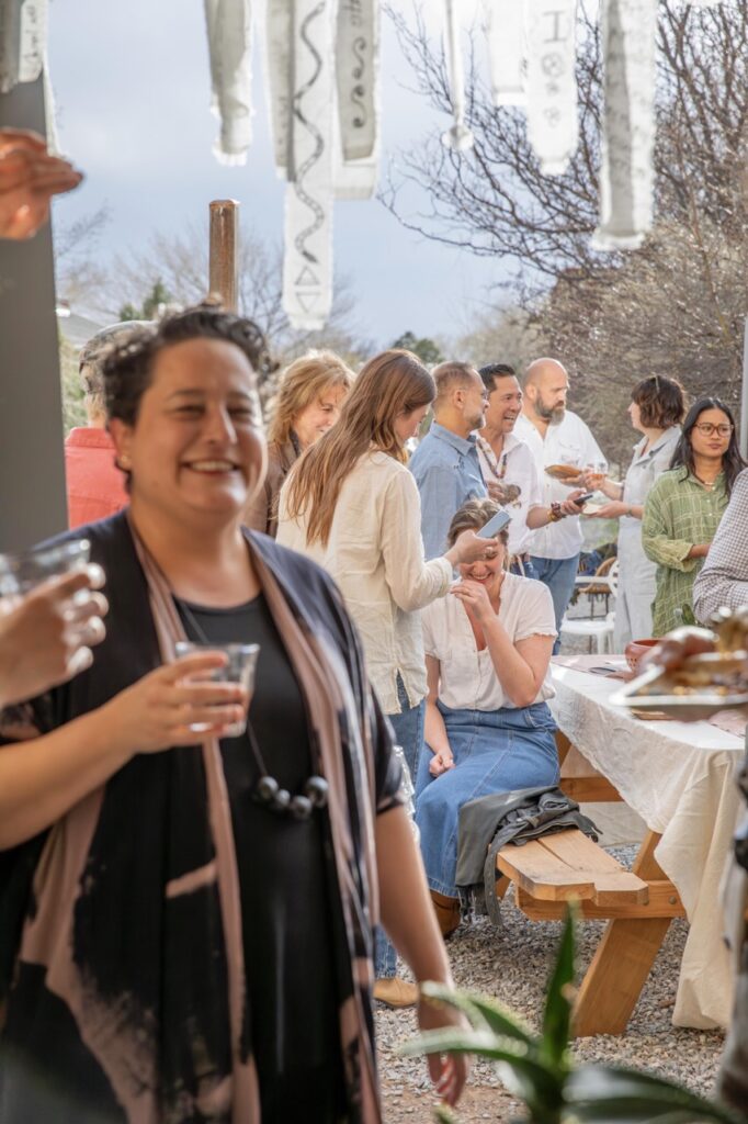 Spring Launch Party 26 TABLE Magazine A woman smiles in the forefront as people talk in the background.