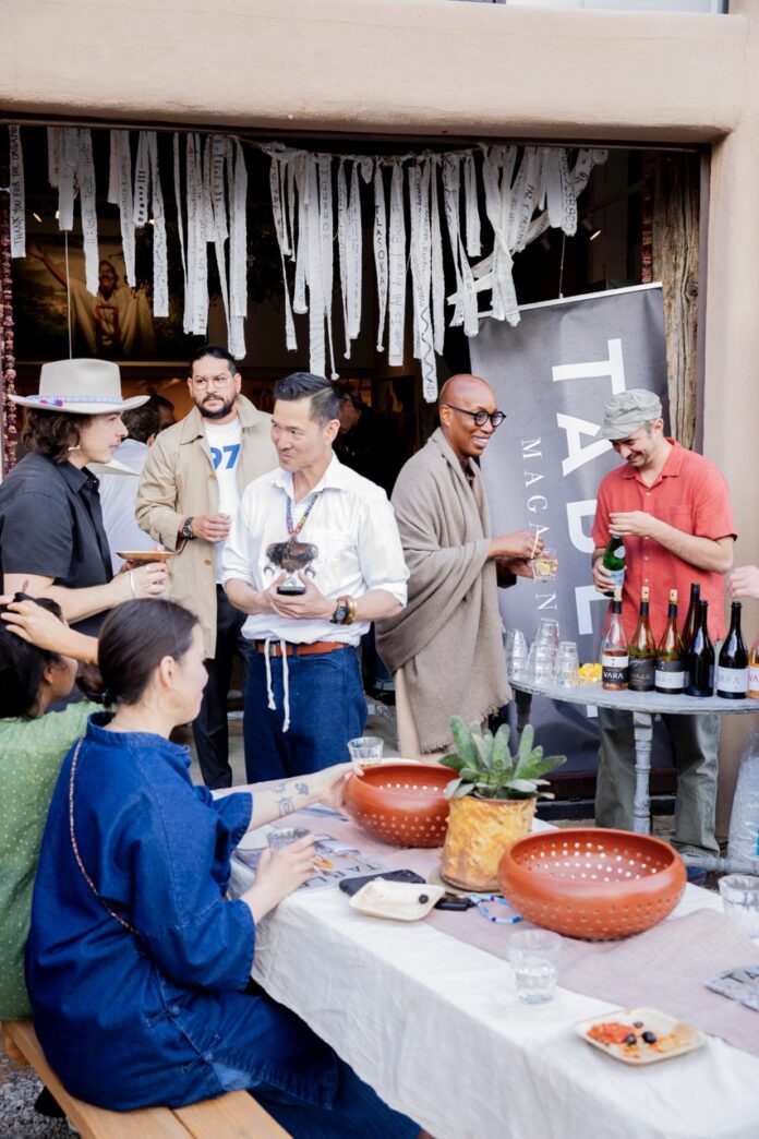 People smile and pour wine behind a picnic table.