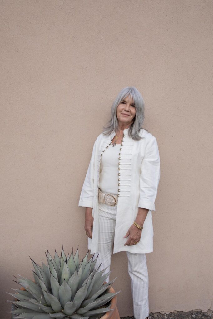 Spring Launch Party 34 TABLE Magazine A woman in white stands in front of a beige wall outside.