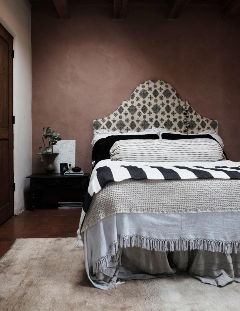 A bedroom with a large bed in the center. The bed has a white and black patterned headboard and is covered in white, gray, and black bedding.