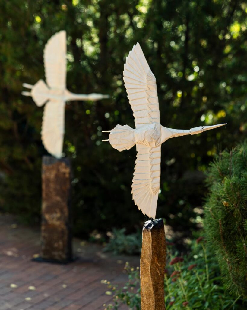 Two white, origami-style swan sculptures are shown in a garden.