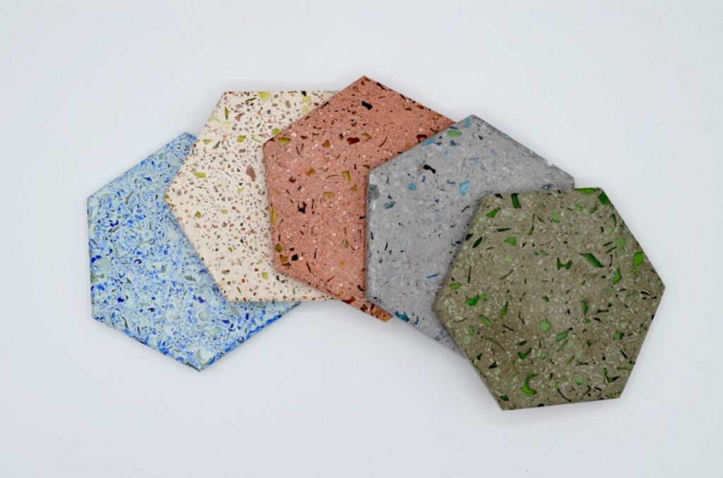 A collection of five hexagon-shaped coasters in various colors and patterns, made from recycled glass.