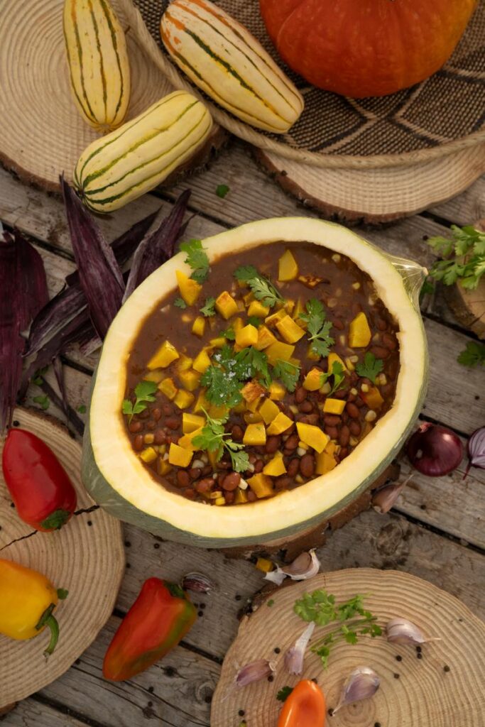 A halved squash filled with a thick brown soup made from squash and beans, and garnished with chopped yellow squash and fresh cilantro.
