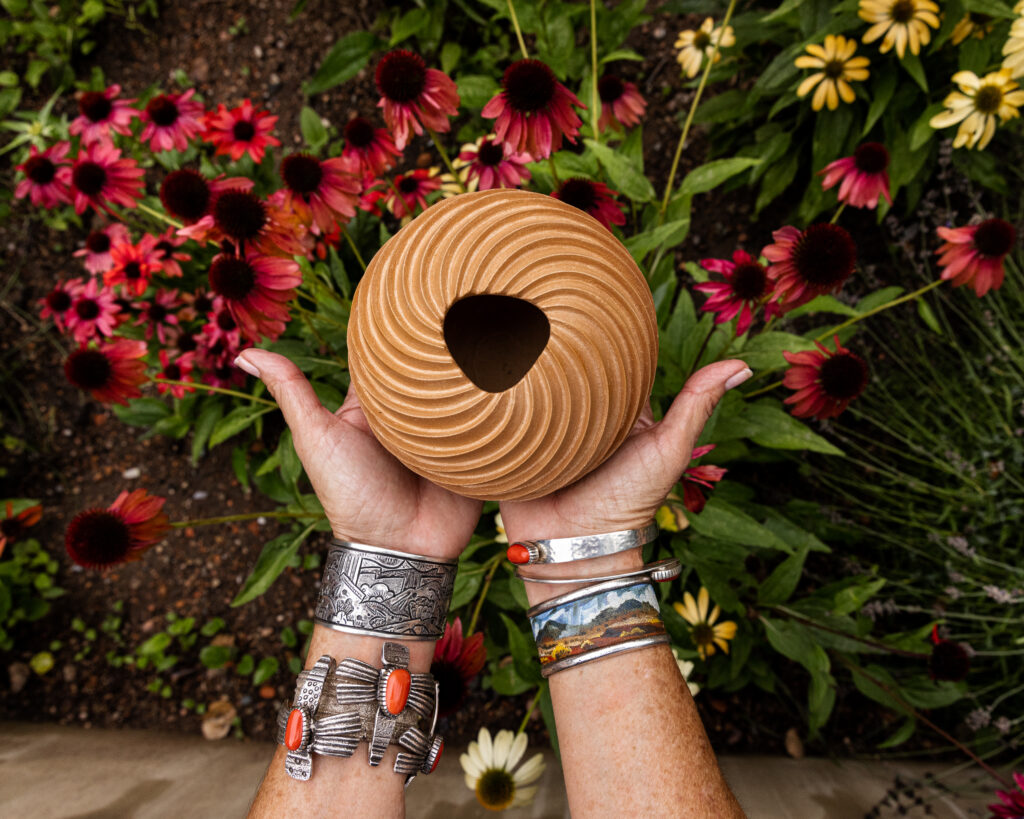 hands holding round brown vase above red and green plants