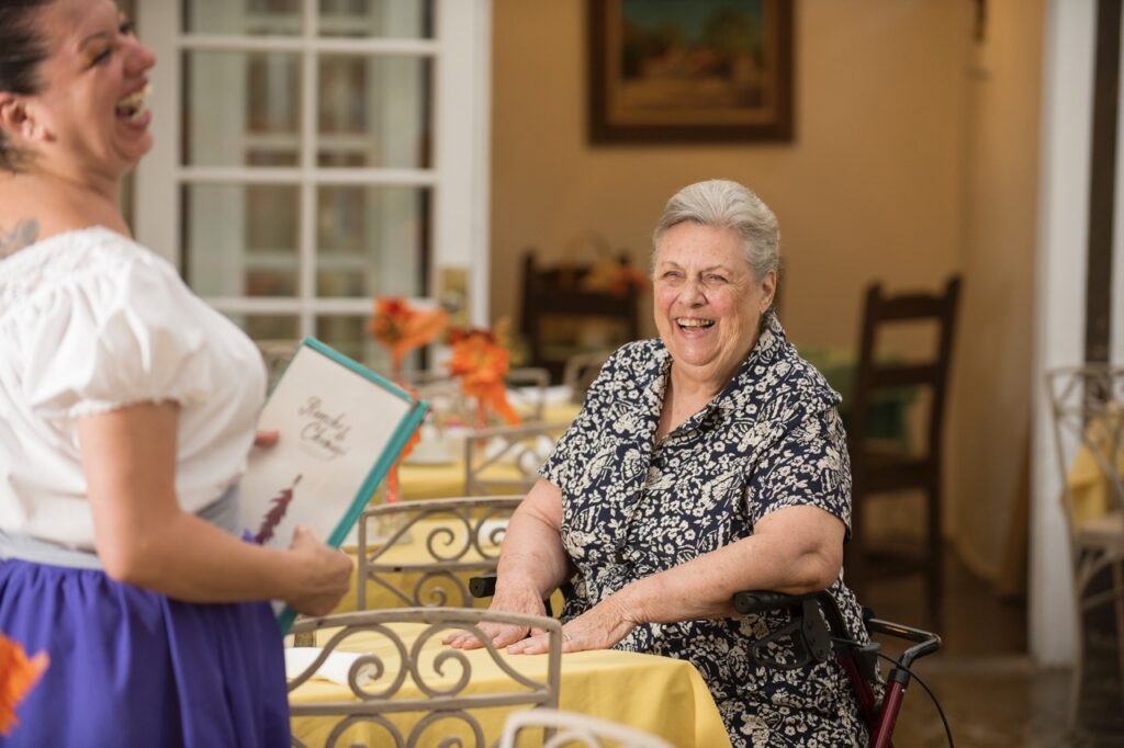 A woman smiles at a yellow table as a waitress laughs nearby.