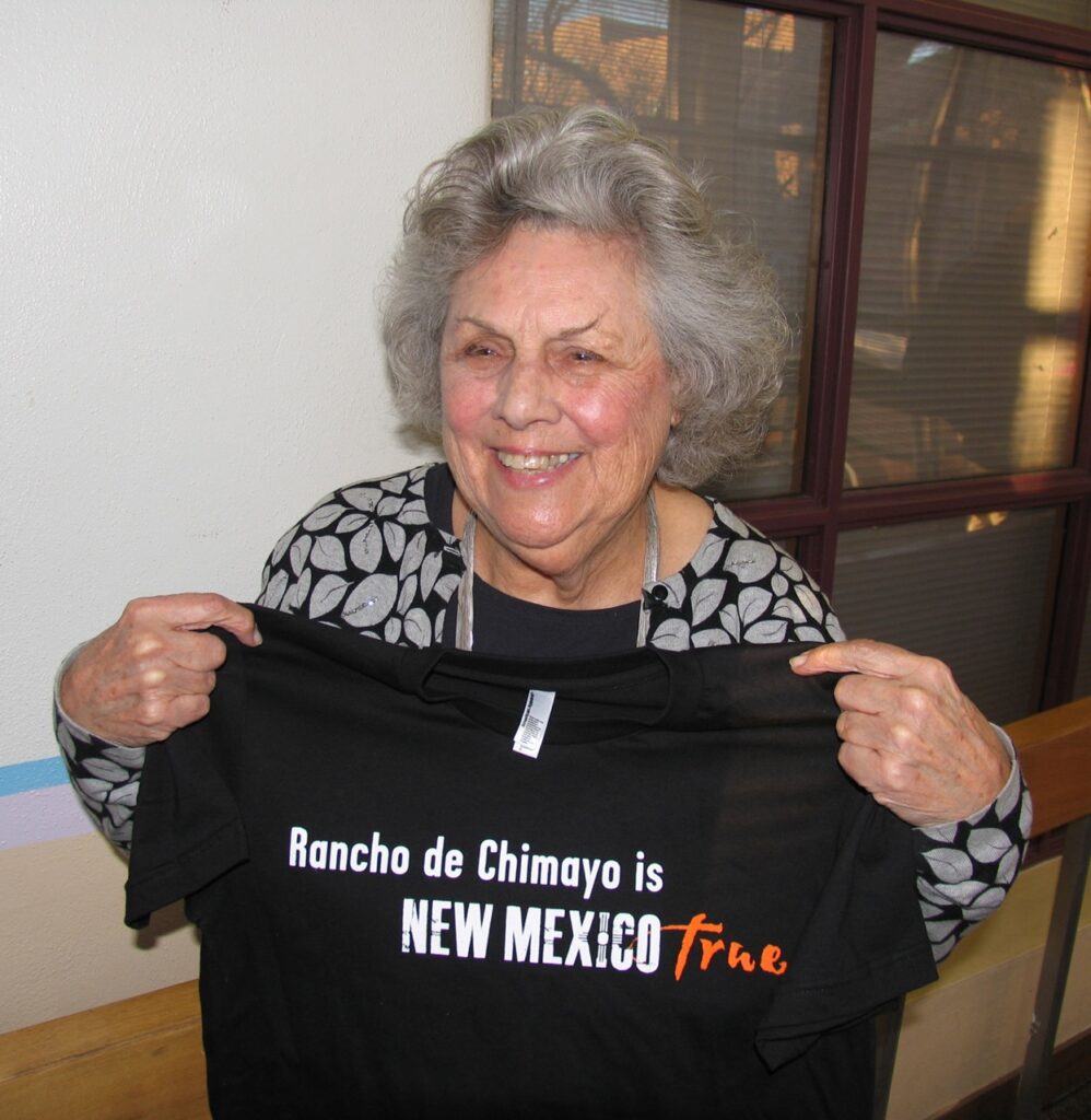Florence Jaramillo holds a black tshirt about New Mexico in front of her, smiling.