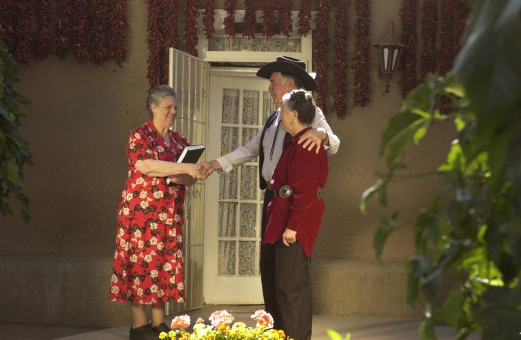 A woman in a red dress shakes hands with an older southern couple.