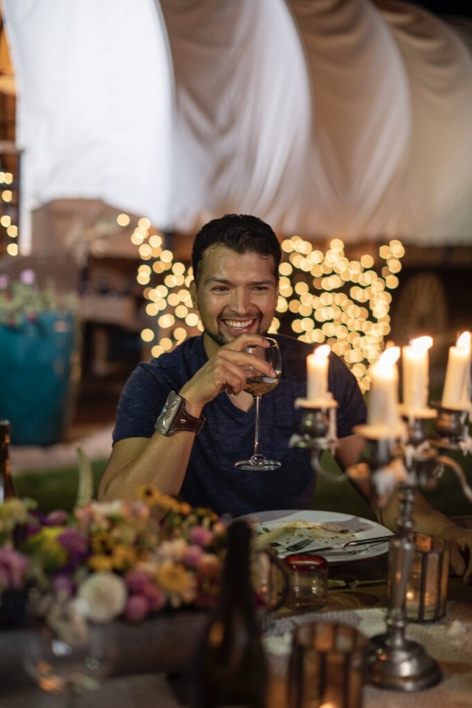 A man holds a wine glass in his hand as he sits at a table outside.