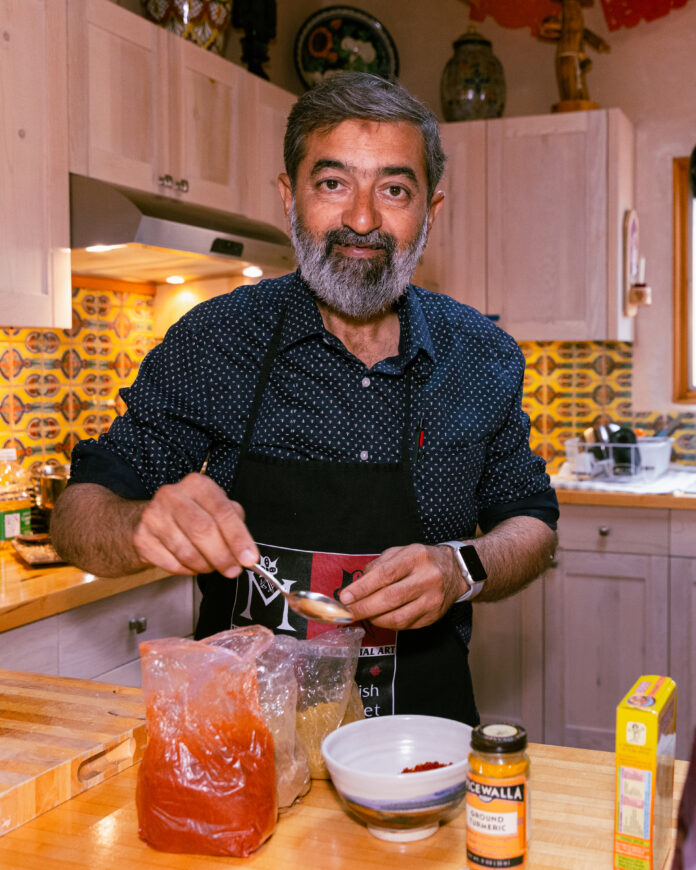 man in kitchen with white cabinets making red sauce
