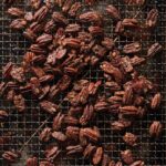A close-up of candied cocktail pecans sprinkled with salt on a metal cooling rack.
