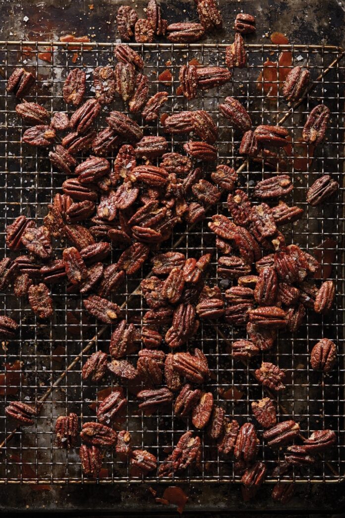 A close-up of candied cocktail pecans sprinkled with salt on a metal cooling rack.