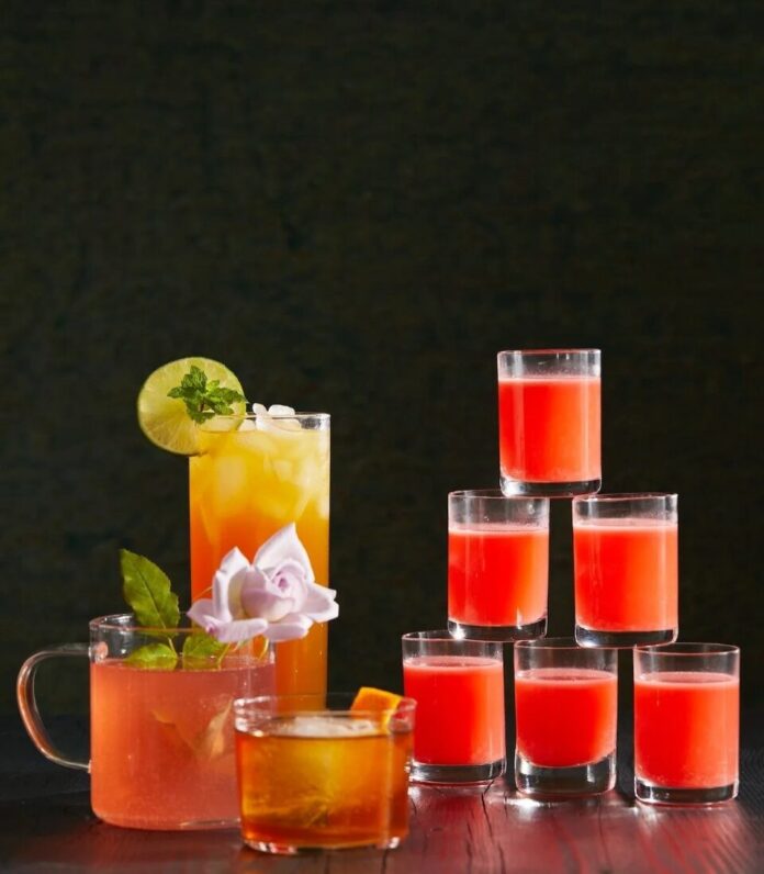 A tall pyramid of small glasses filled with a vibrant red-orange liquid, with a variety of other cocktails on the left.