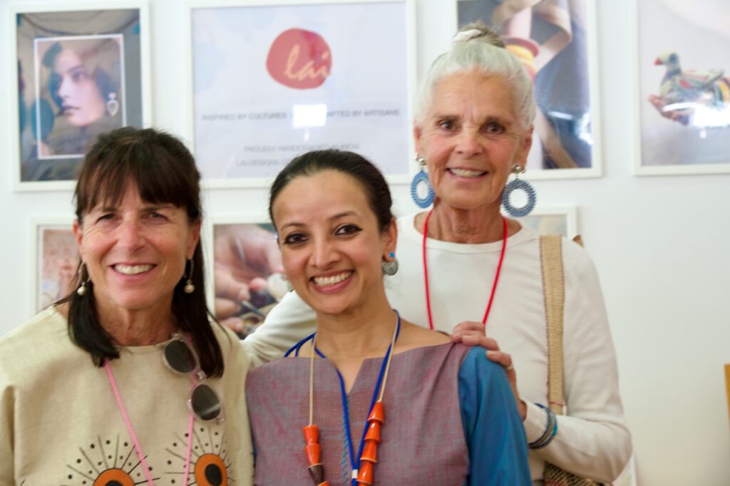 Puja Bhargava/Craft Stories/Lai, (with Ali McGraw & friend) India, Booth 93, 7/11/25_Crosby Three women stands together in front of a white wall.