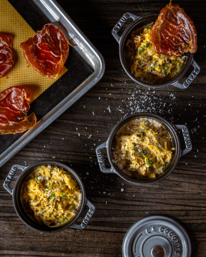 Three small ramekins hold a casserole type recipe with meat being placed over top.