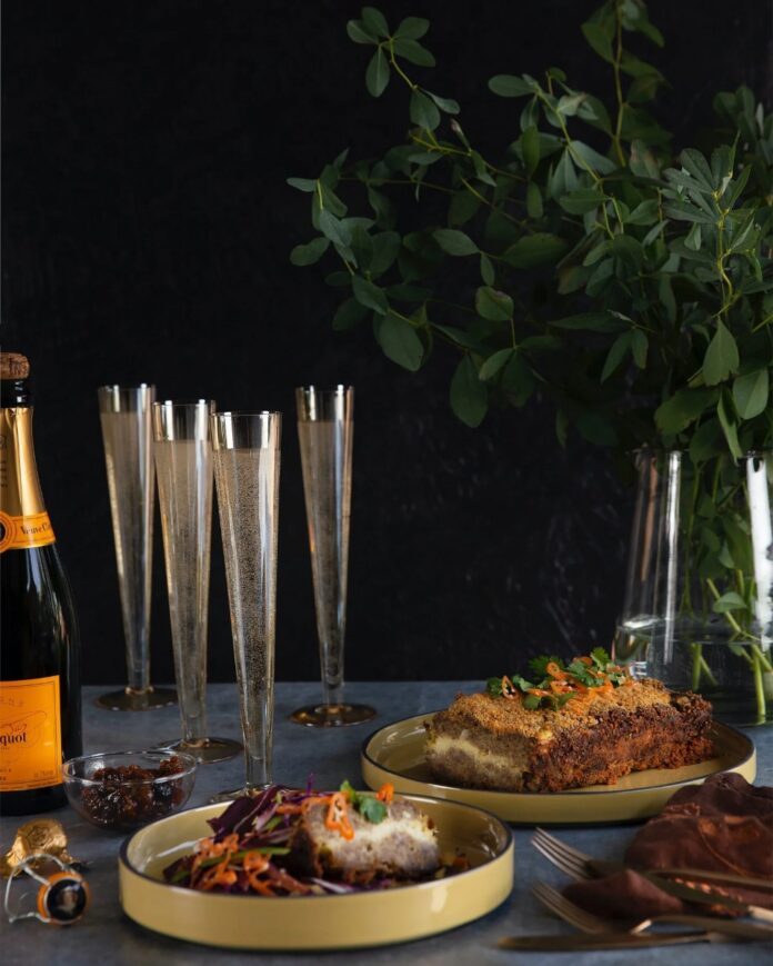 two yellow plates with slices of layered meatloaf, accompanied by flutes of champagne and a glass bottle on a table.