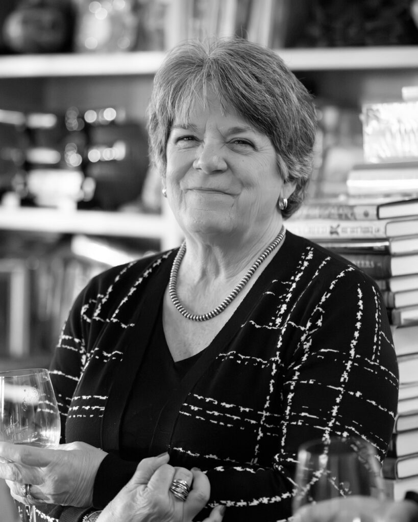 A woman in a plaid shit with her arms crossed and a wine glass in her hand.