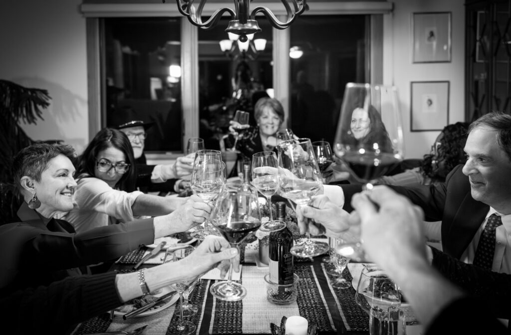 A group of people at a dining table cheers wine glasses.