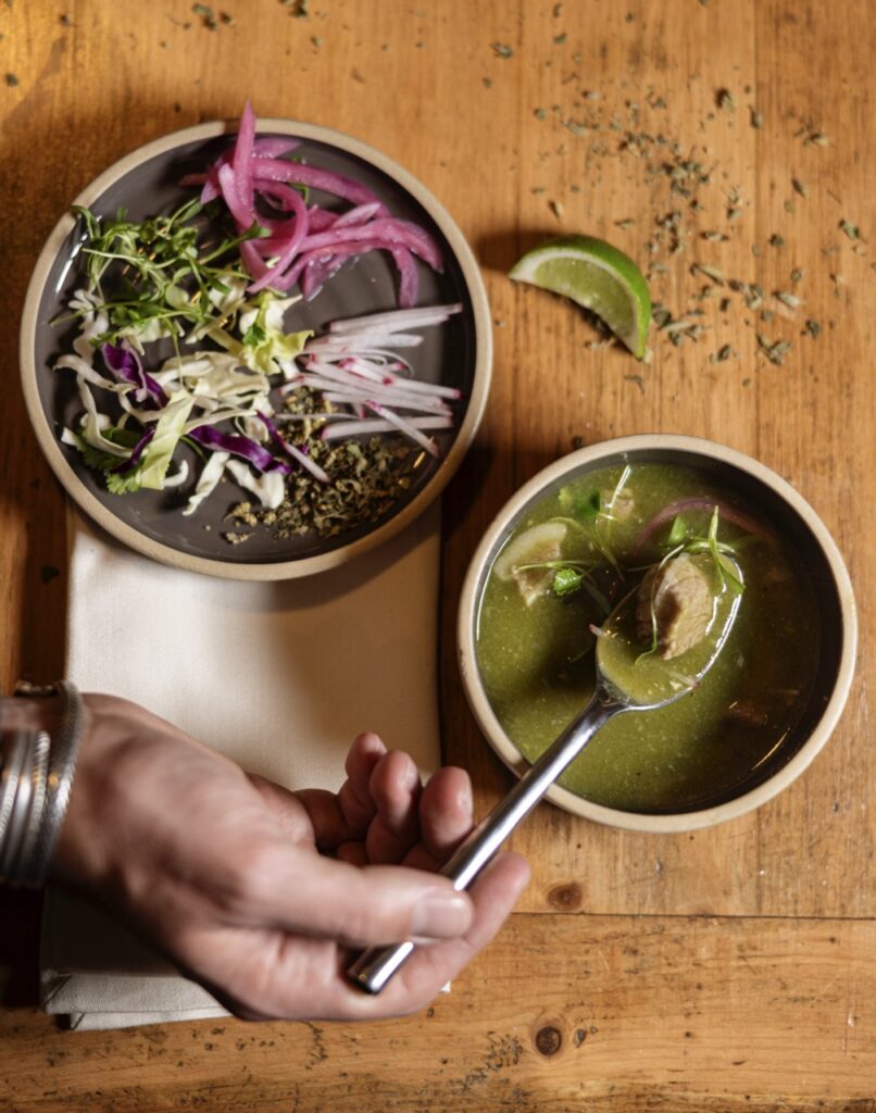 A salad on a plate beside a bowl of green soup.