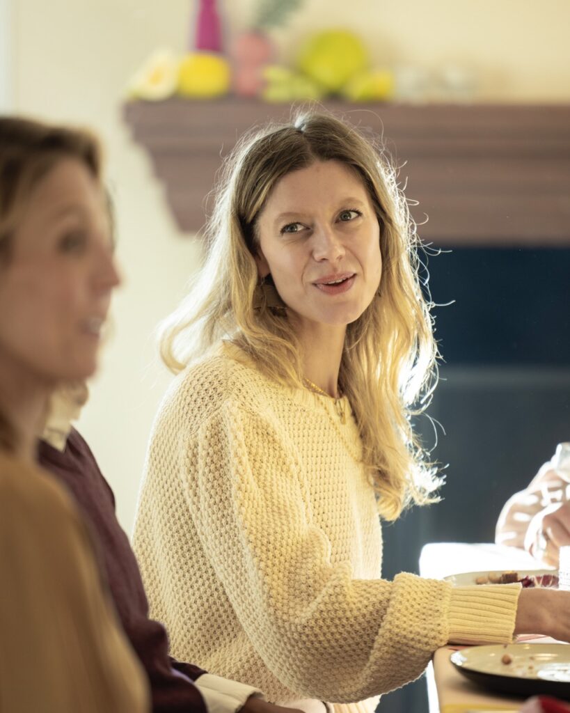 A woman in a white sweater and blonde hair sitting at a table.