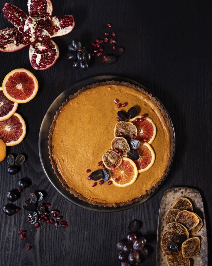 A round brown tart with blood oranges and lemons on top as a garnish.