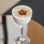 A chilled Coquito cocktail in a coupe glass, garnished with a star anise and cinnamon, for a Puerto Rican holiday drink.
