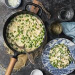 A creamy pot of Risi e Bisi (Venetian rice and peas) and a serving on a blue and white plate, garnished with Parmesan cheese and a side of chopped onion.