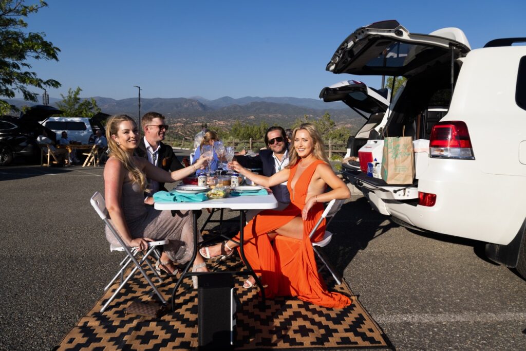 Audience Experience Portrait Series July 4 2025 Santa Fe Opera A group of people cheers glasses at a fold out table in a parking lot.