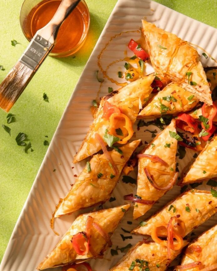 Savory Romesco Baklava triangles drizzled with hot honey and topped with sliced peppers and parsley, ready to serve.