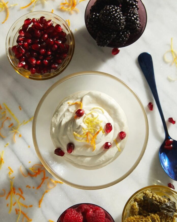 Sugar-Free Cashew Cream with lemon zest, pomegranate seeds, and fresh blackberries and raspberries on a marble counter.
