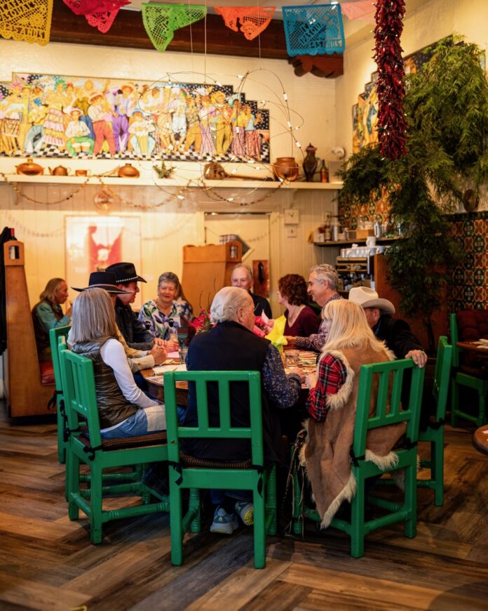 A Seat at the Table at Cafe Pasqual’s, people eating around a table sitting in green chairs