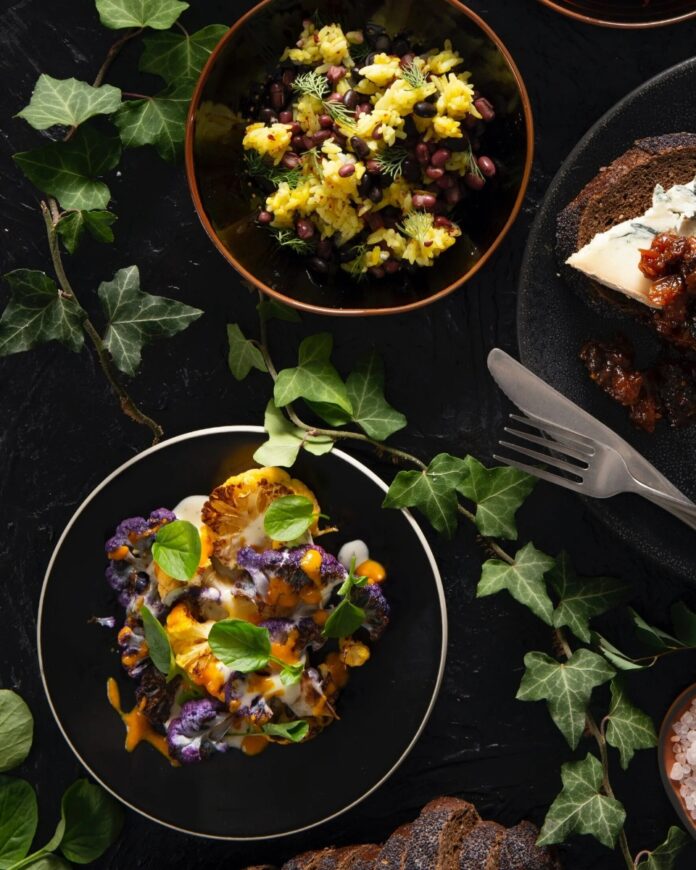 Roasted cauliflower with ginger and turmeric on a black plate, drizzled with a creamy sauce and garnished with fresh greens.