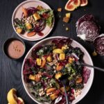 A big white bowl of salad with various toppings and black eyed peas beside a small pink plate with the salad on it.