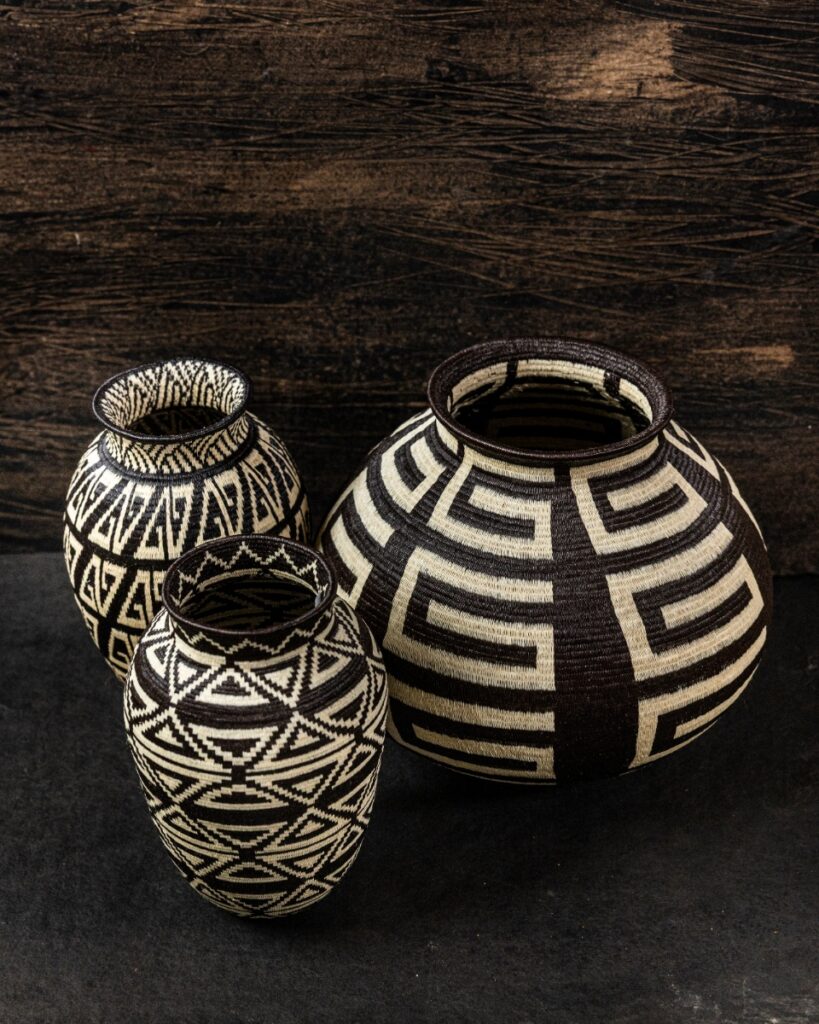 Three handwoven black and white woven baskets with bold geometric patterns, made by Indigenous artists from the Darien Rainforest, on a dark background.