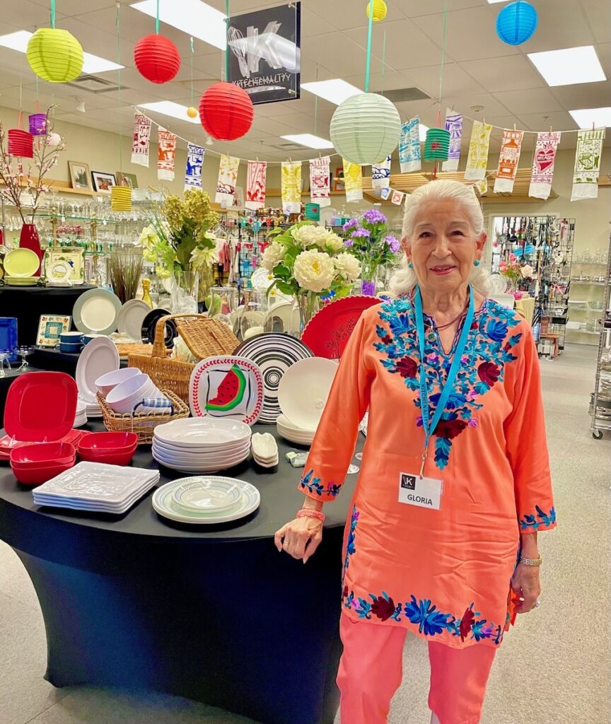 A woman in pink and blue stands beside a table.