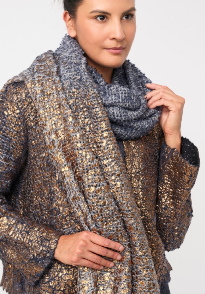 A woman modeling a cozy knit Avant Toi metallic gold and gray jacket with a matching chunky knit scarf around her neck.