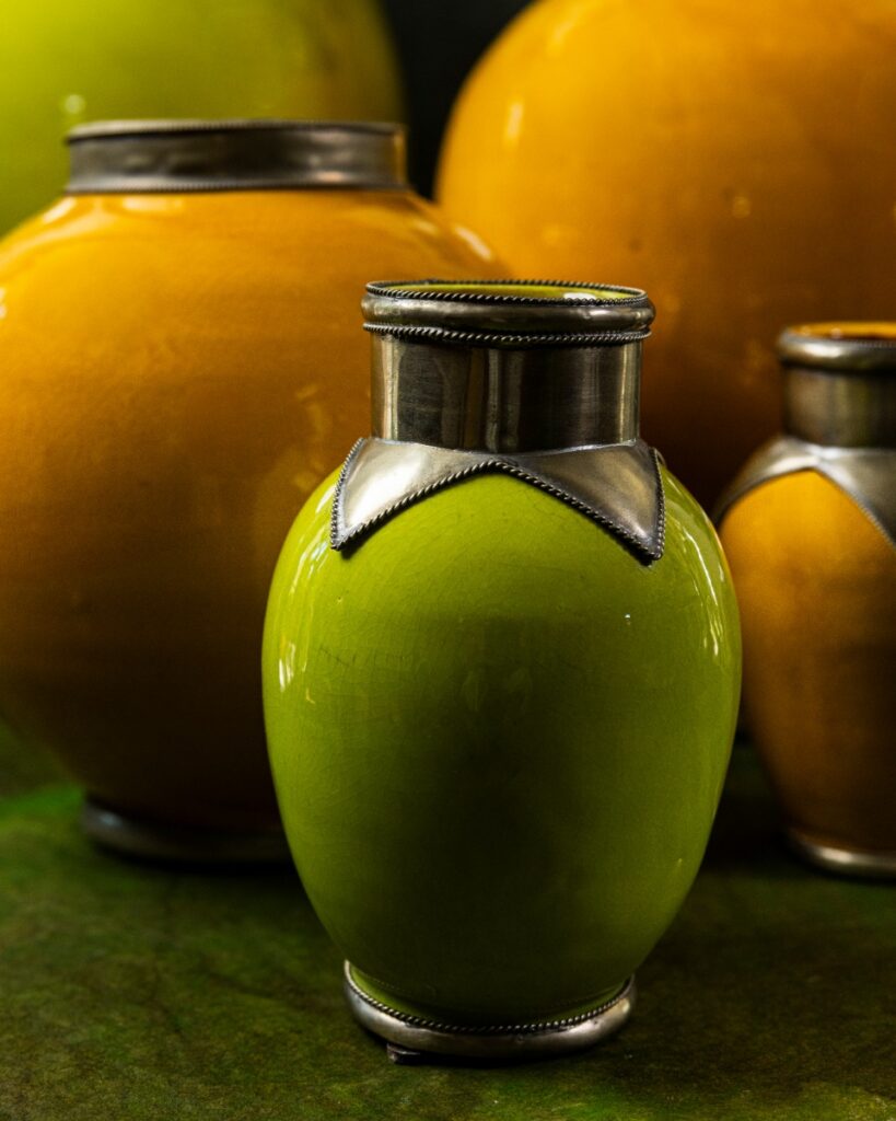 A Moroccan ceramic vase in Granny Smith apple green with a silver embossed metal collar, next to a large ochre yellow vase.