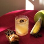 A chai masala good luck mimosa with grapefruit juice sits on a red table top with a star anise garnish in the glass and citrus slices nearby.