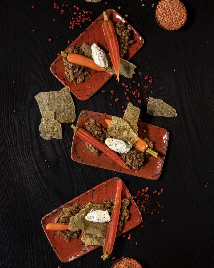 Three orange rectangular plates with pickled baby carrots, smoked labneh, and lentils.