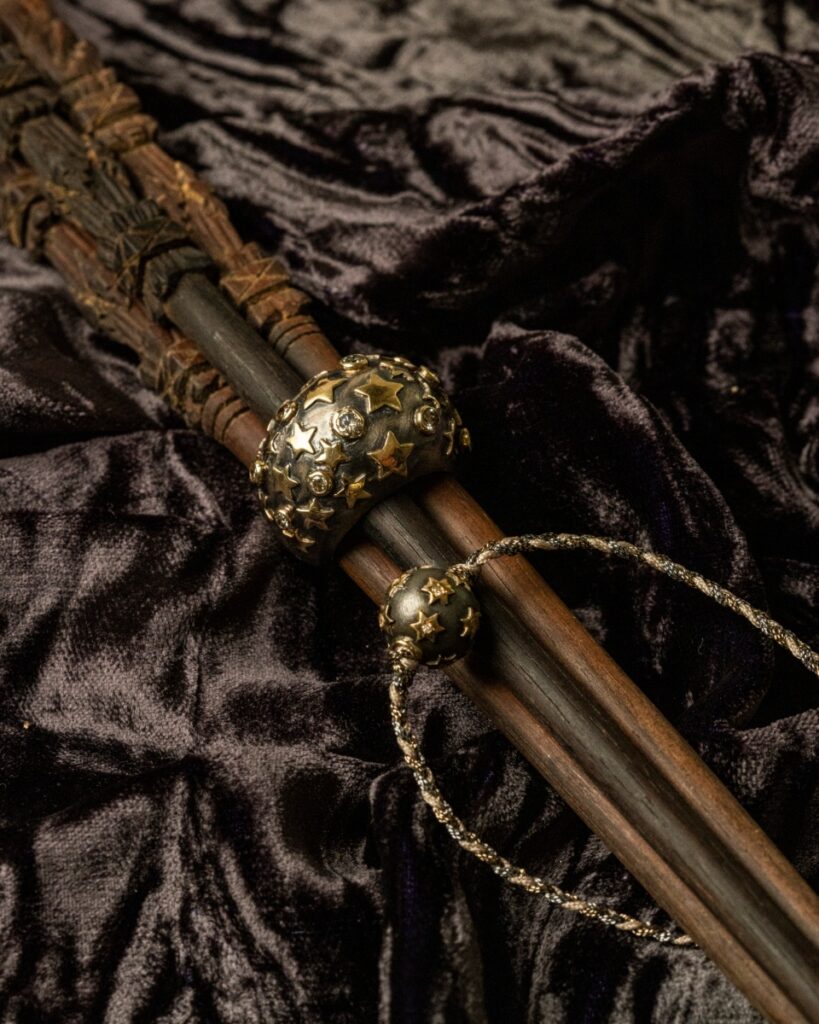 A dark, oxidized silver ring featuring a star pattern in 10K yellow gold, set on carved wooden shafts and a black velvet cloth.