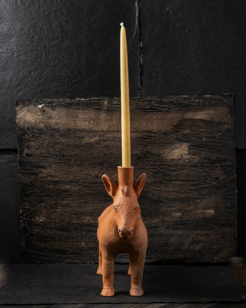 A terracotta horse candle holder by Oaxacan potter José García Antonio with a tall yellow taper candle, against a dark, textured background.