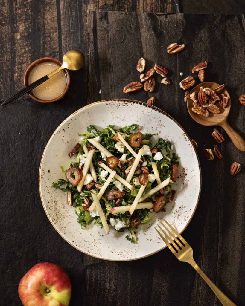 A white palte holds a salad with kale, brussels sprouts, and apple sticks from The Compound Restaurant.