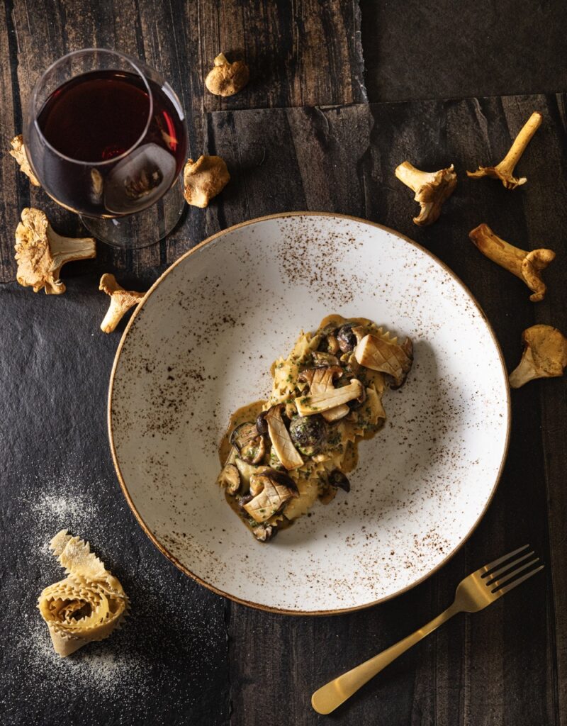 A white plate with a mushroom stroganoff in the center surrounded by mushrooms on the table.