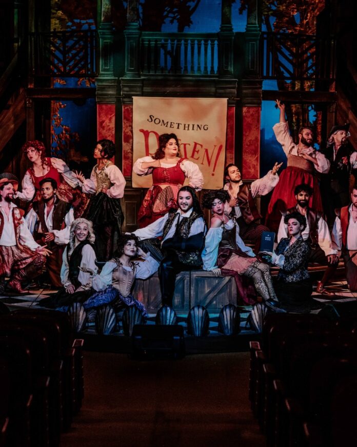 A group of actors in victorian wear pose on a stage.