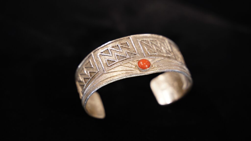 Tufa-cast sterling silver cuff bracelet by Mathew Lovato with geometric lightning motifs and a round piece of bright red Apple coral.