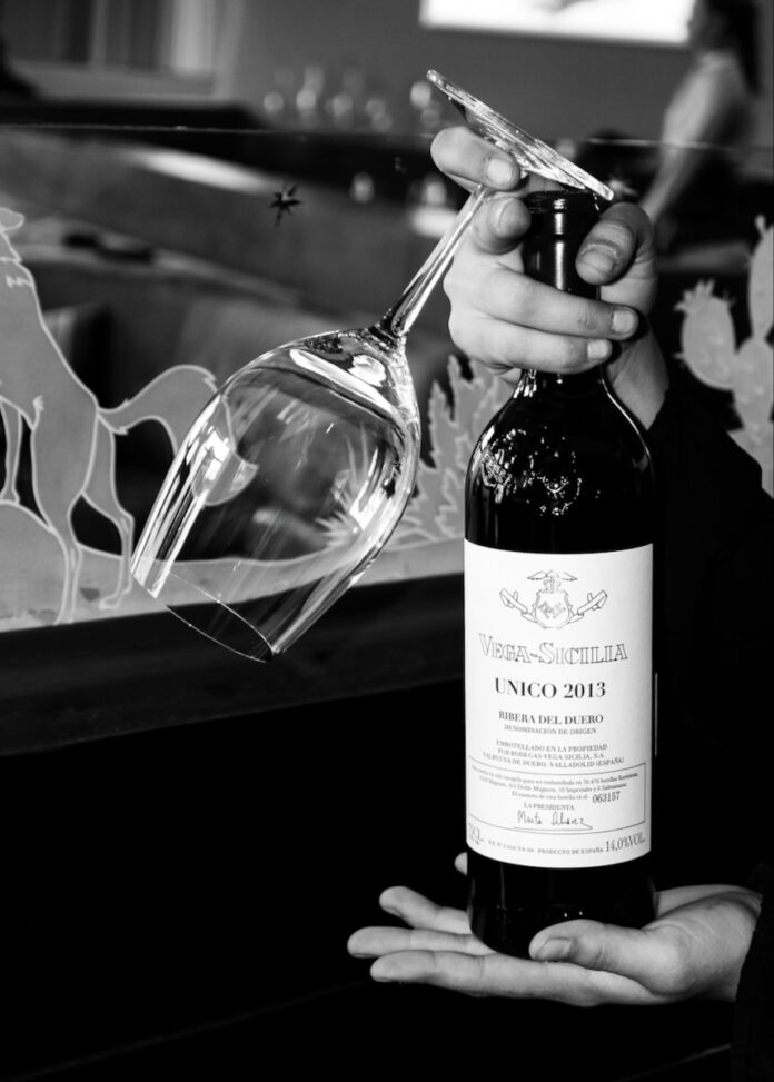 A person holds a wine bottle and a wine glass upside down in their hand.