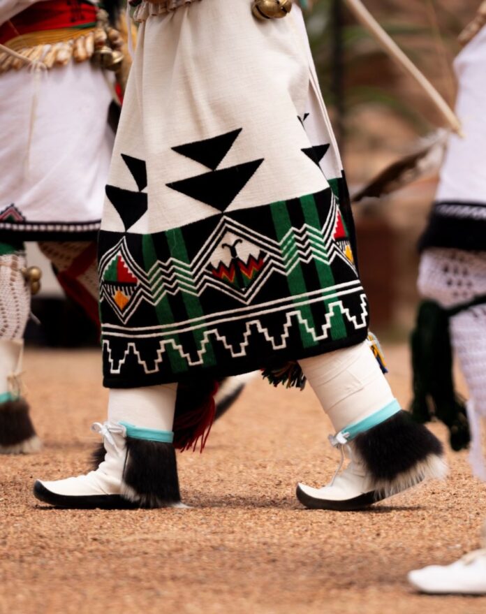 A Native dancers feet as they walk forward in traditional clothing.