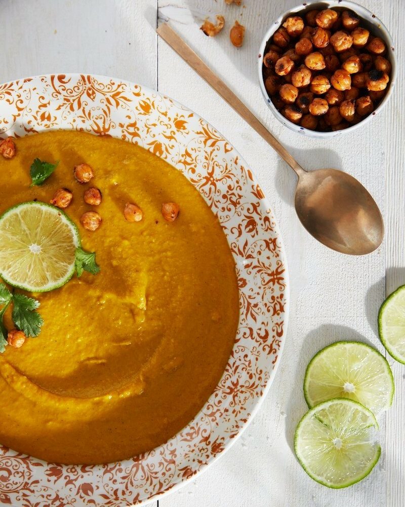 Allergen-free Golden Soup in a plate; a spoon, pieces of lemon, and chickpeas on the side.