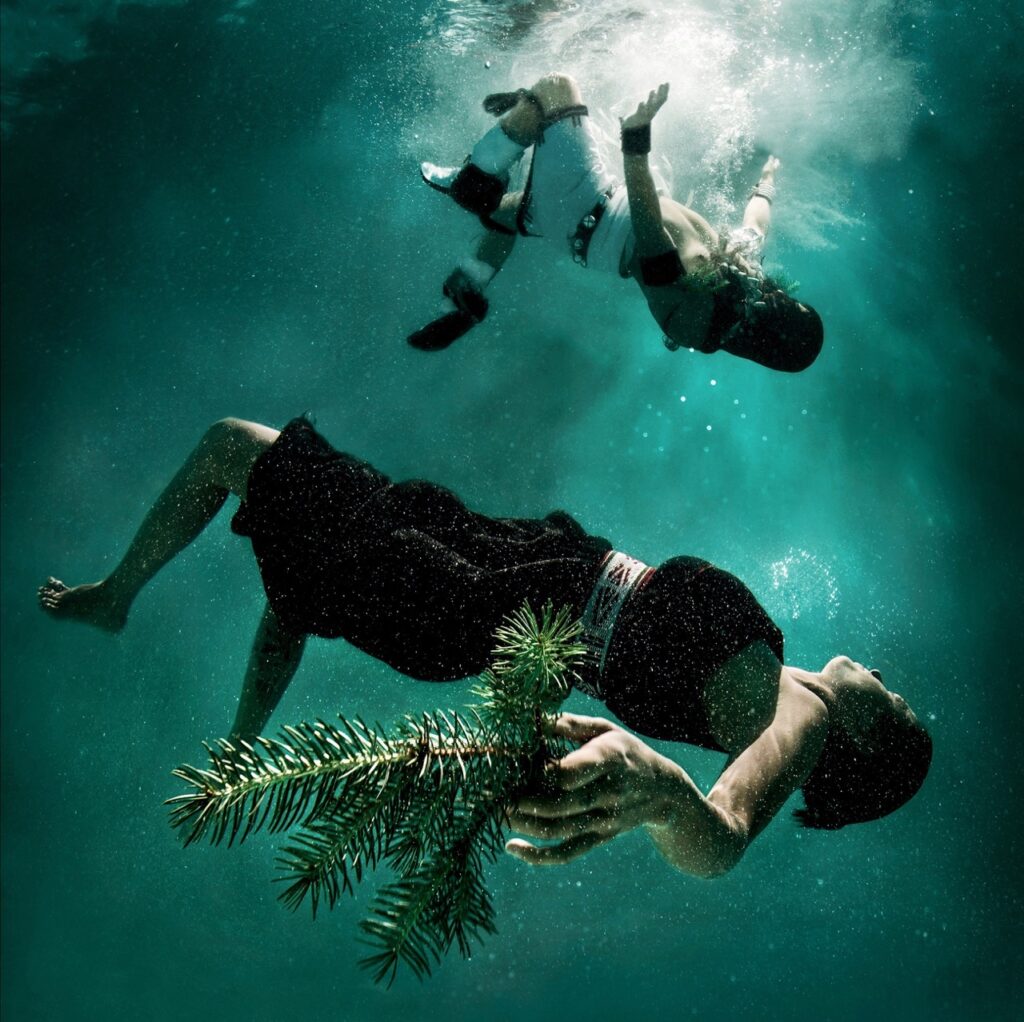 People floating in the water with pieces of trees in their hands.