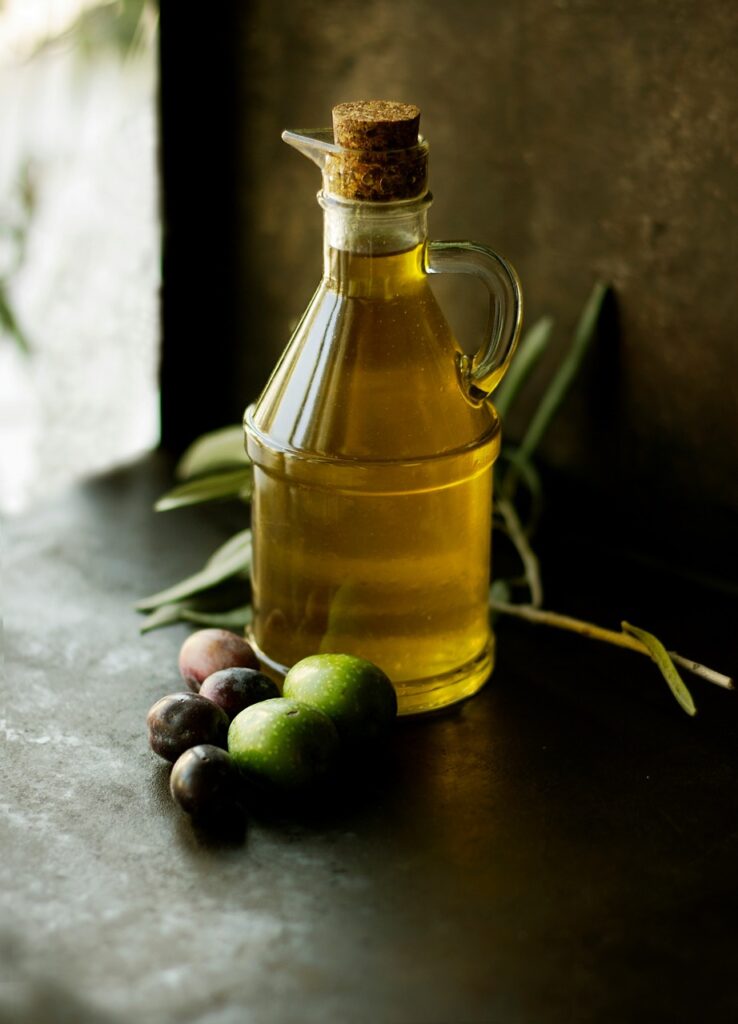 A bottle of olive oil sits on a table with olives around it.
