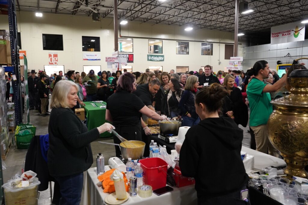 A group of people gather around a table to receive a sample of soup.